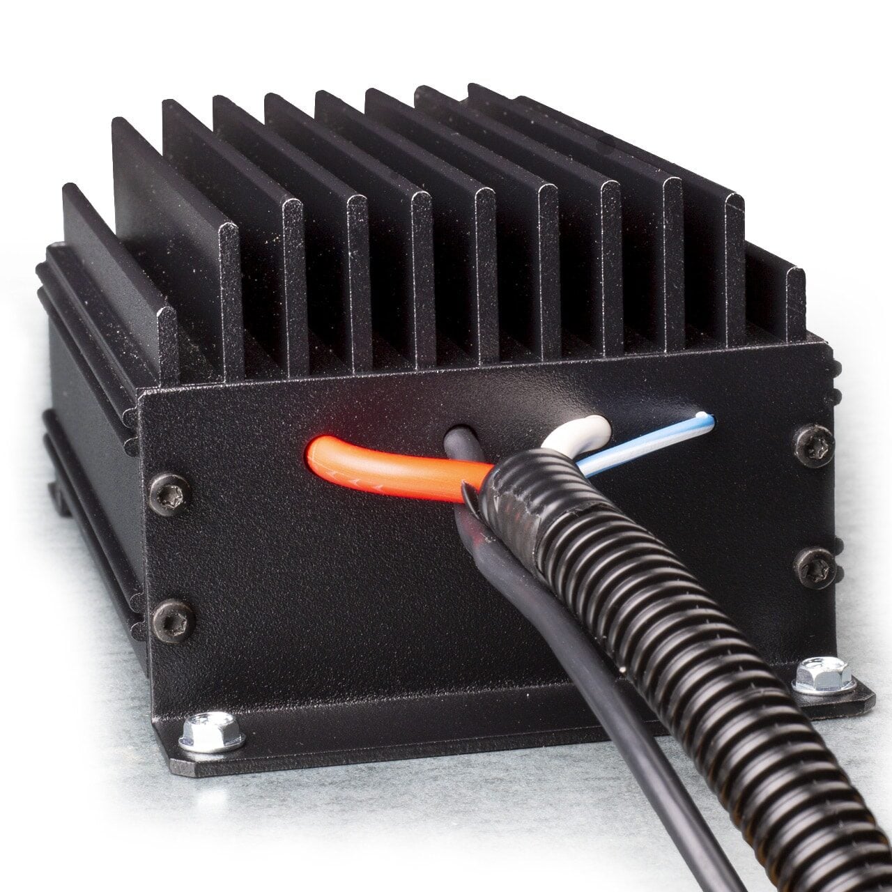 A black metal electronic device with cooling fins and several colored wires (red, white, blue, and black) connected at the back, with a black protective cable sleeve covering part of the wires.