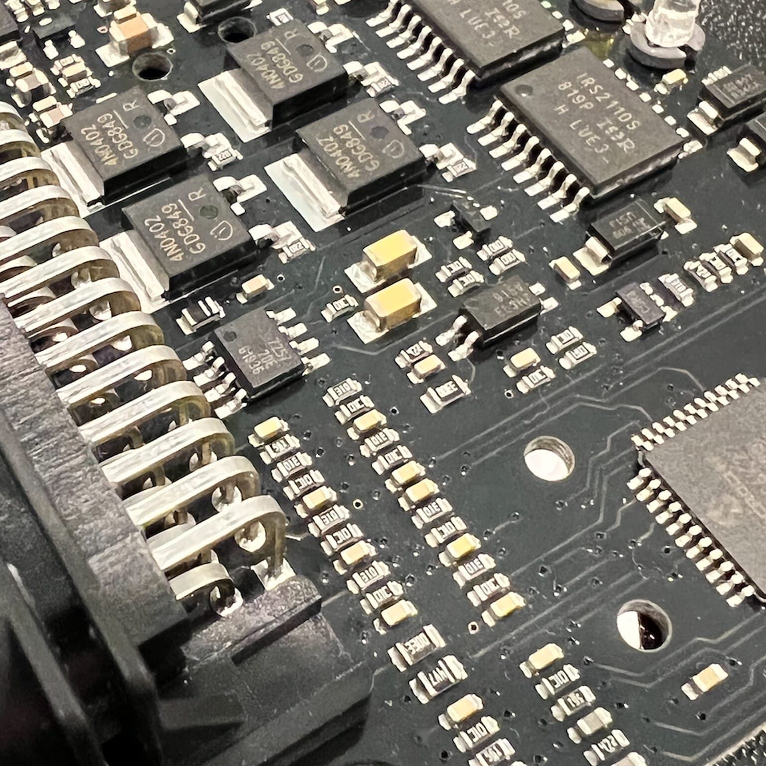 Close-up of an electronic circuit board showing various components, including resistors, capacitors, integrated circuits, and soldered connections on a black PCB.