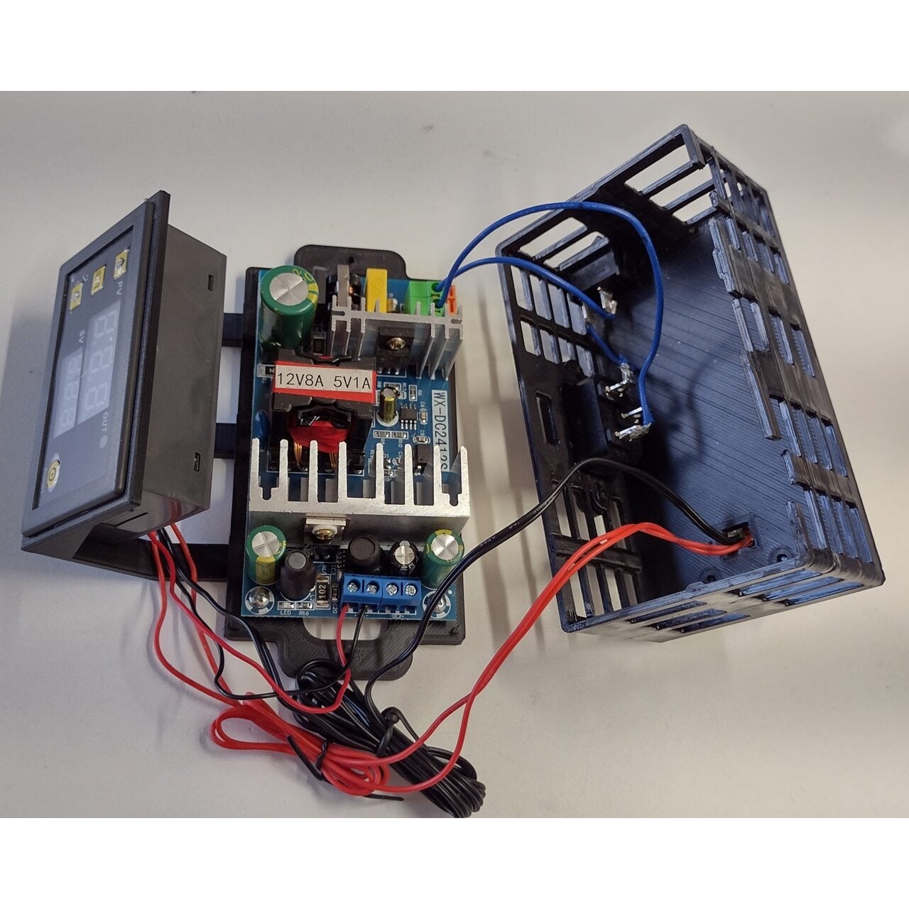 Open electronic device showing a display panel connected by red and black wires to a circuit board with a transformer, capacitors, and heatsinks, next to a partially open plastic casing.