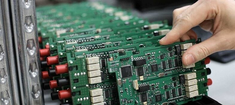 A hand is placing or inspecting green printed circuit boards lined up in rows, featuring various electronic components like chips and connectors.